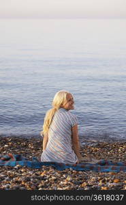 Young woman sitting on beach, back view