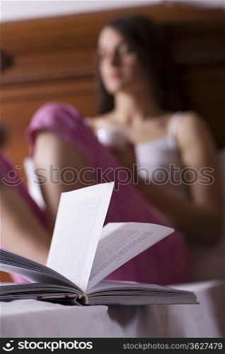 Young woman sitting on bed and reading book, portrait