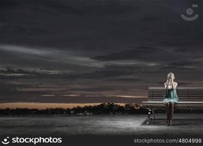 Young woman sitting on bench closing eyes with palms. Alone with fears