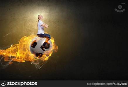 Young woman sitting on burning soccer ball. Woman ride ball