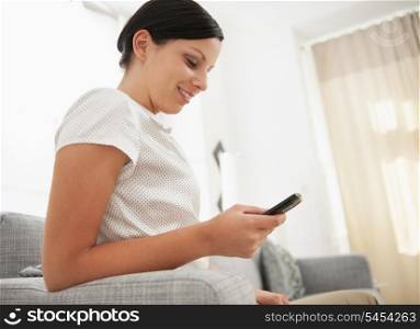 Young woman sitting on couch and writing sms