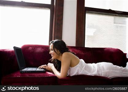 Young woman sitting on couch using laptop