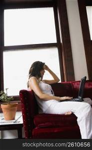 Young woman sitting on couch using laptop