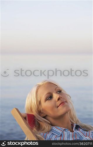 Young woman sitting on deckchair on beach, close up, portrait