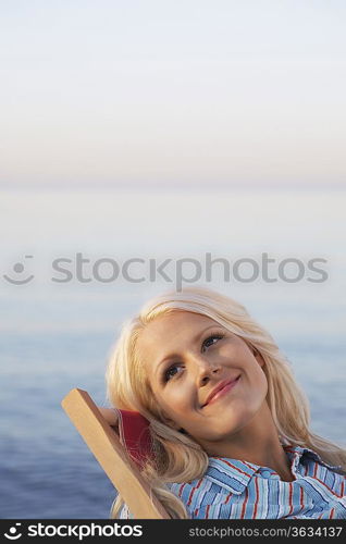 Young woman sitting on deckchair on beach, close up, portrait