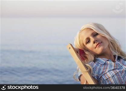 Young woman sitting on deckchair on beach, close up, portrait