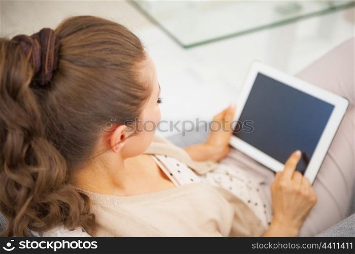 Young woman sitting on divan and using tablet pc . rear view