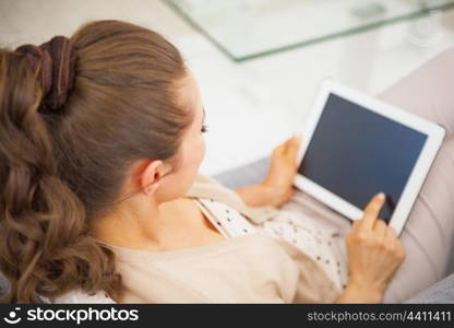 Young woman sitting on divan and using tablet pc . rear view