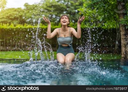 young woman sitting on edge of swimming pool and playing water splashing