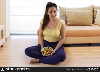 Young woman sitting on floor with a bowl of salad at home