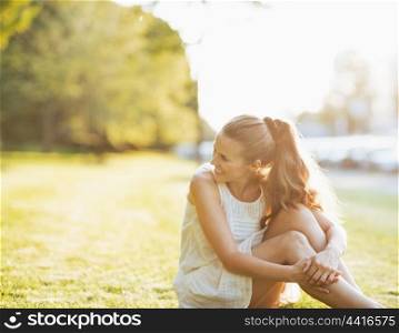 Young woman sitting on grass in park and looking on copy space