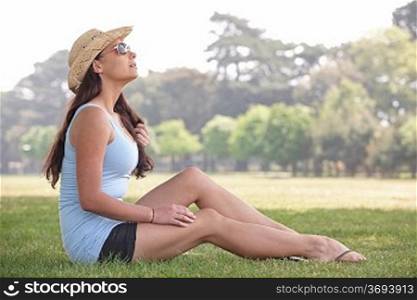 young woman sitting on grass in park enjoying the sunshine