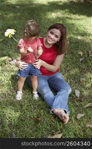 Young woman sitting on grass with her daughter and smiling