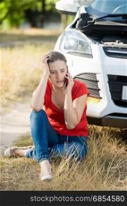 Young woman sitting on ground and leaning on broken car