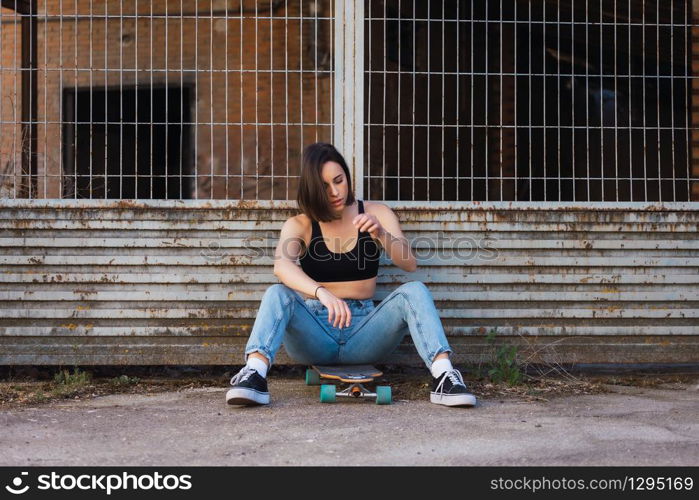 Young woman sitting on her skate in an old industrial street