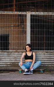 Young woman sitting on her skate in an old industrial street