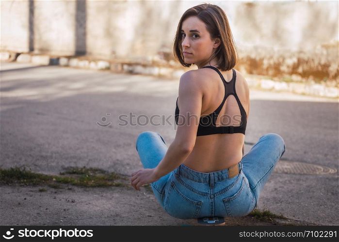 Young woman sitting on her skate in an old industrial street
