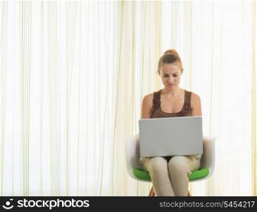 Young woman sitting on modern chair and using laptop