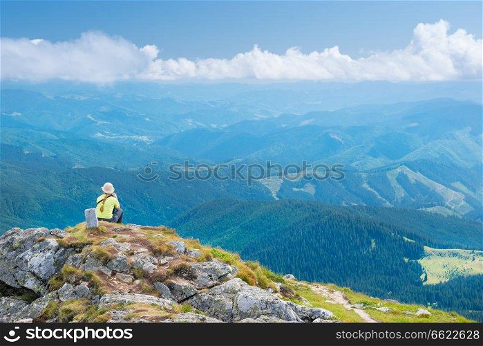 Young woman sitting on mountains cliff and looking at blue hills