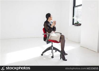 Young woman sitting on office chair with coffee