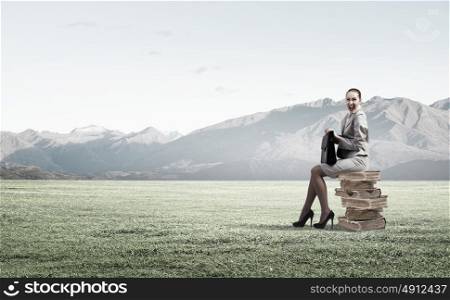 Young woman sitting on pile of books with book in hands. Taking break from office