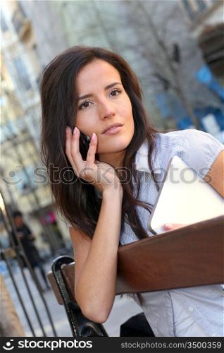 Young woman sitting on public bench with mobile phone