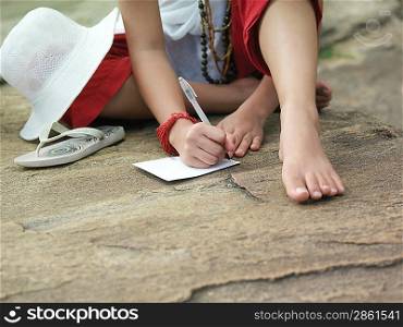 Young woman sitting on rock writing low section