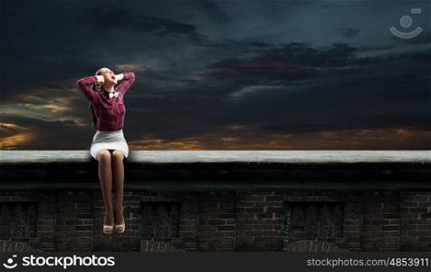 Young woman sitting on roof and covering ears with hands