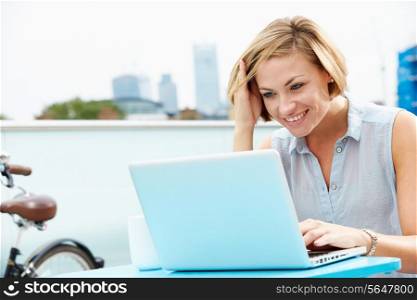 Young Woman Sitting On Roof Terrace Using Laptop