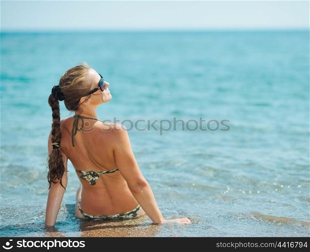 Young woman sitting on sea coast. rear view