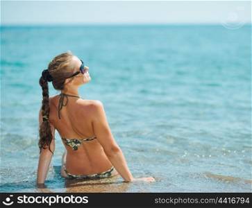 Young woman sitting on sea coast. rear view
