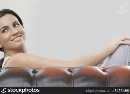 Young woman sitting on sofa against gray background
