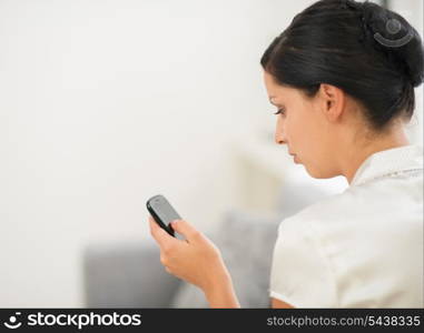 Young woman sitting on sofa and reading sms on mobile phone. Rear view