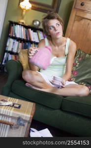 Young woman sitting on sofa at home drinking tea