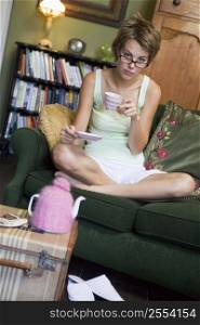 Young woman sitting on sofa at home drinking tea