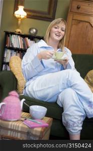 Young woman sitting on sofa at home drinking tea