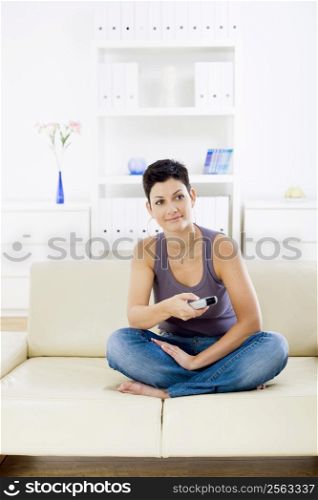 Young woman sitting on sofa at home watching TV.