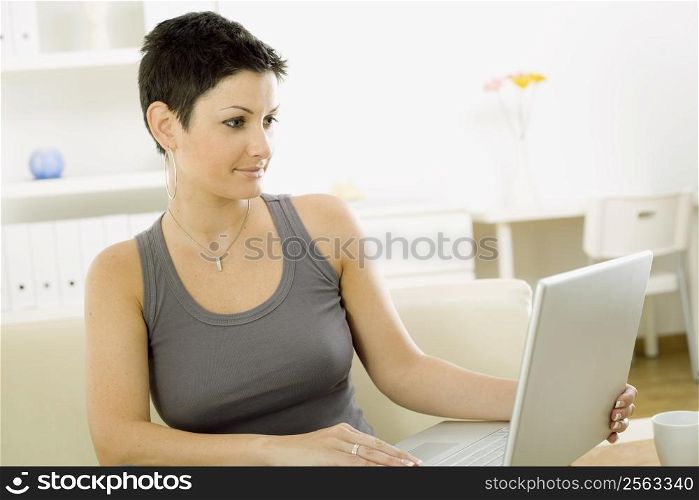 Young woman sitting on sofa at home working on laptop computer.