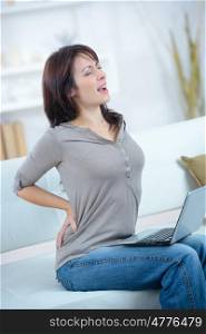 young woman sitting on sofa suffering from back ache