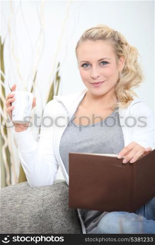 young woman sitting on sofa with photograph album and mug of coffee