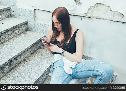 Young woman sitting on stairway reading smartphone texts