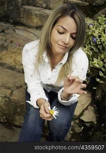 Young woman sitting on steps and picking petals of a flower