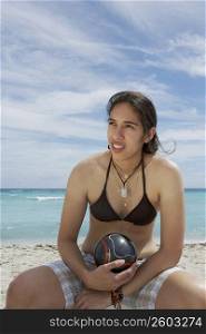 Young woman sitting on the beach and holding a soccer ball