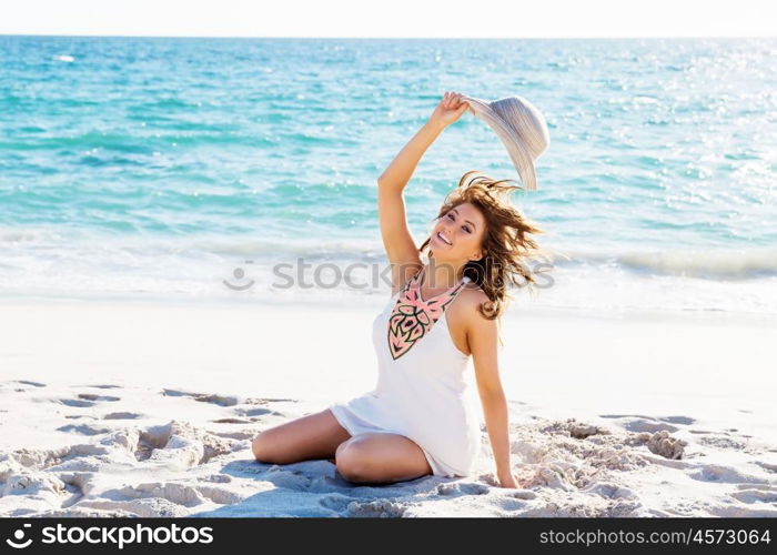 Young woman sitting on the beach. Portrait of young pretty woman with hat sitting on the beach