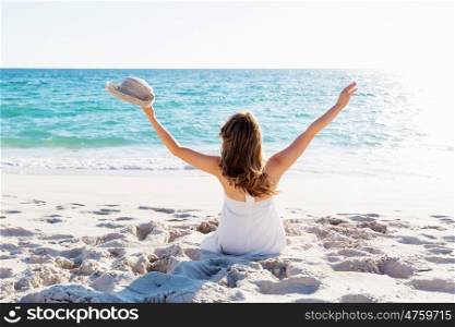 Young woman sitting on the beach. Portrait of young pretty woman with hat sitting on the beach