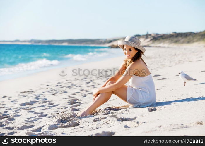 Young woman sitting on the beach. Portrait of young pretty woman with hat sitting on the beach