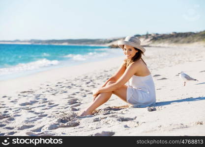 Young woman sitting on the beach. Portrait of young pretty woman with hat sitting on the beach