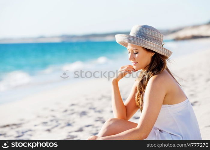 Young woman sitting on the beach. Portrait of young pretty woman with hat sitting on the beach