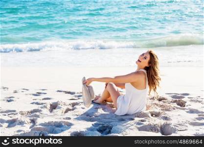 Young woman sitting on the beach. Portrait of young pretty woman with hat sitting on the beach