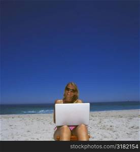 Young woman sitting on the beach with a laptop